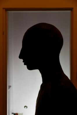 Dunkle Silhouette einer Kopf- und Büstenskulptur im Profil vor einem beleuchteten Türrahmen aus der Serie Fester Schatten von Matilde Romagnoli. 